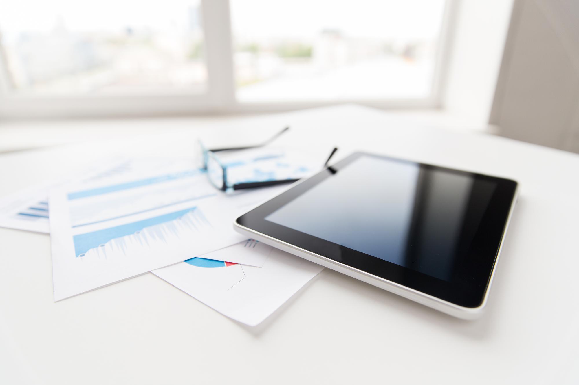 Workspace with reports and tablet displaying financial graphs